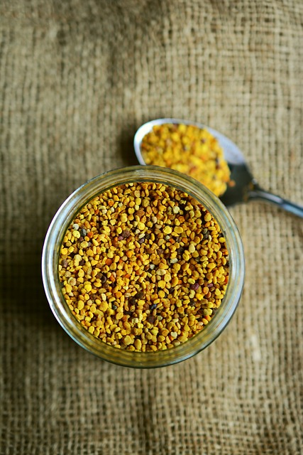 An image of a jar and a spoon filled with bee pollen on a table. 
