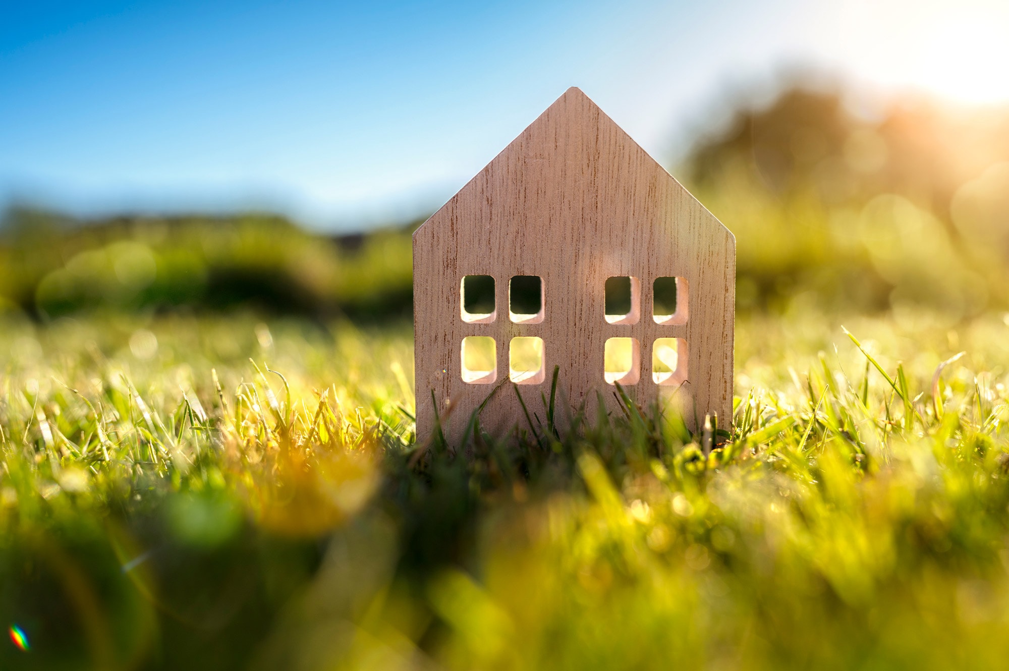 A wooden house model on a sunlit lawn, representing the dream of building your own home with the help of Land Loans in Australia.