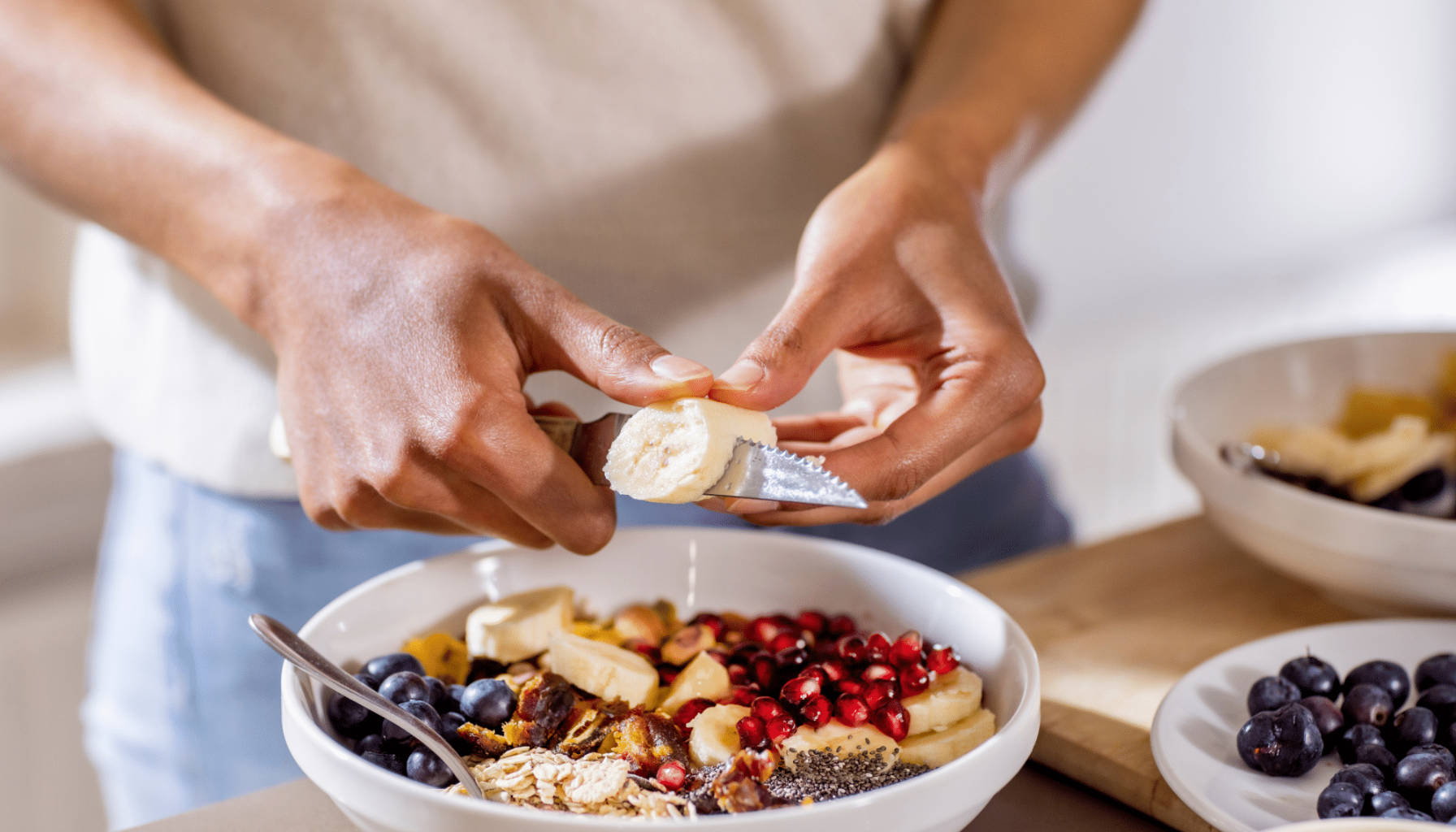 Person skjærer banan over frokostbolle med havregryn og frukt.