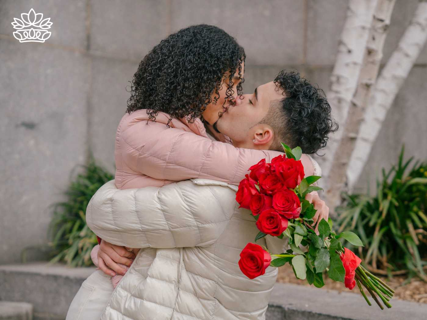 A couple embracing and kissing outdoors while holding a bouquet of red roses, from the Gifts Under R500 Collection at Fabulous Flowers and Gifts, including keywords such as simple, women, advertisement, notebook, chat, and skin.