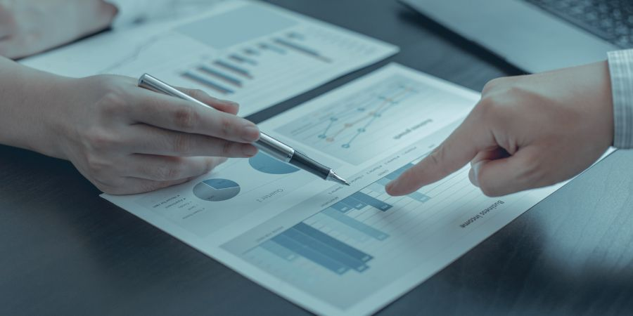 2 people pointing at graphs on a desk