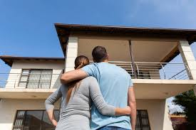 A couple standing in front of a house, looking at it thoughtfully as they consider buying it.