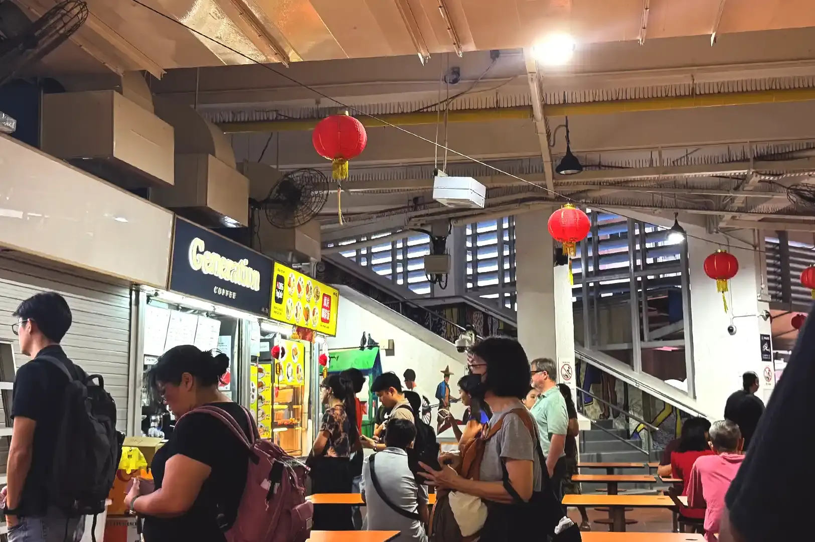 The vibrant corridor of Tekka Market with red Chinese New Year lanterns hanging overhead and people lining up beside the Generation Coffee stall.