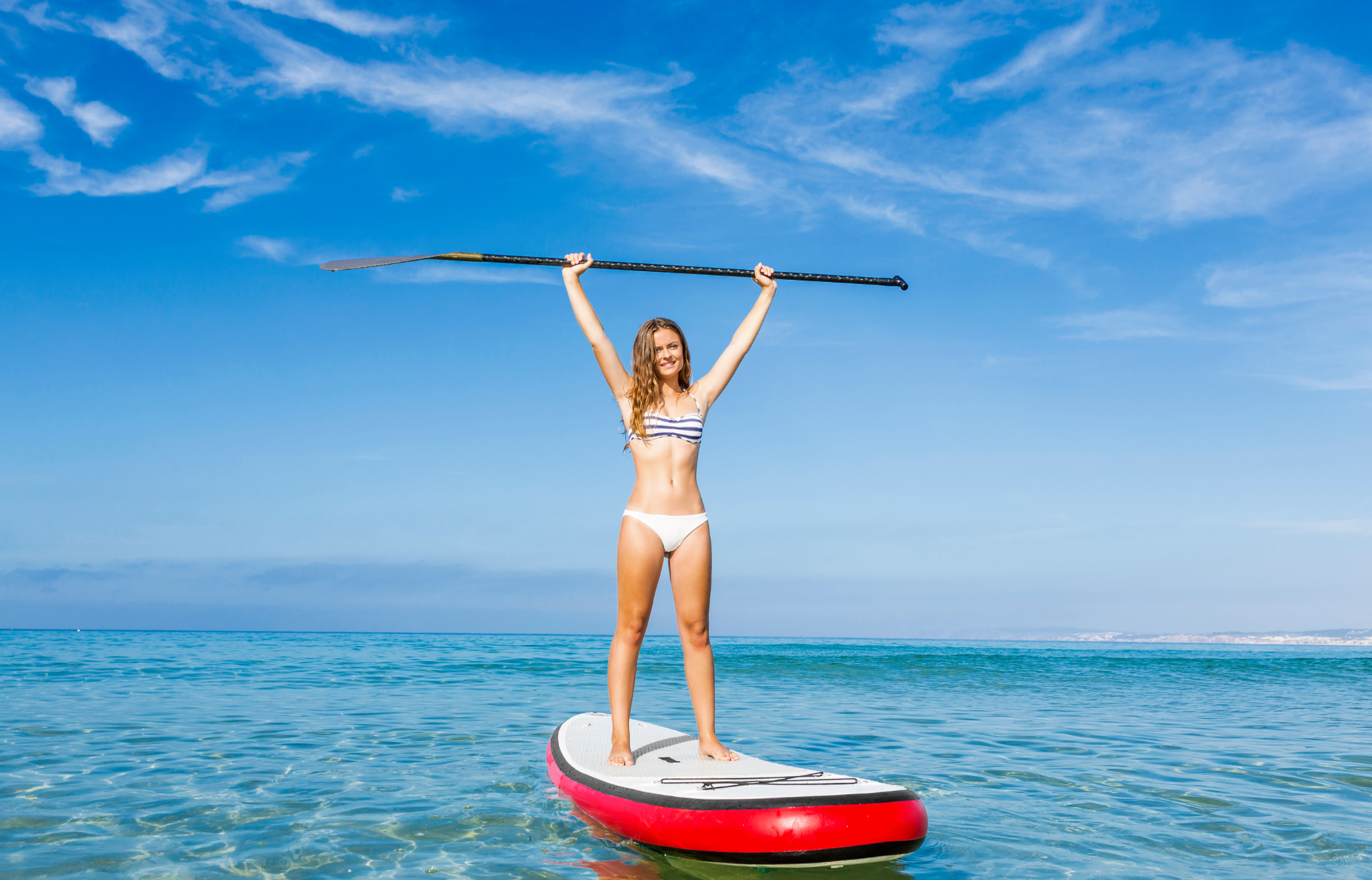 Woman on paddle board lifting paddle above her head - Adventure Wise Travel Gear