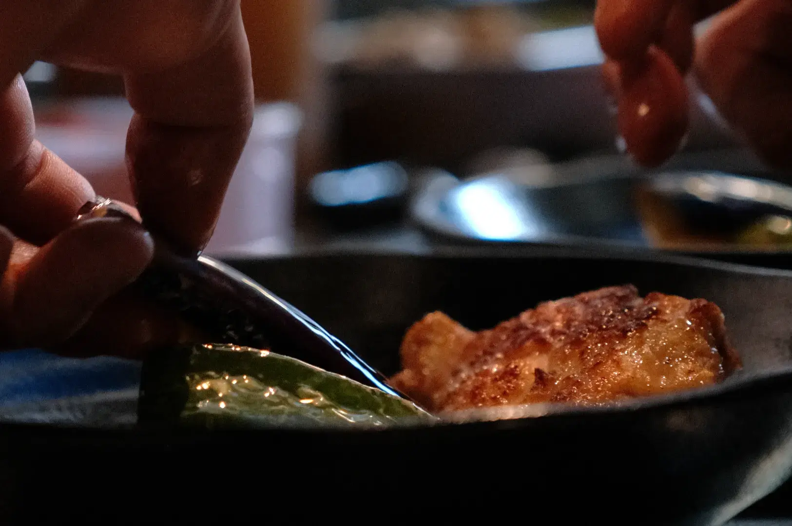 A close-up of hands using a fork to pick up a piece of food from a black dish.