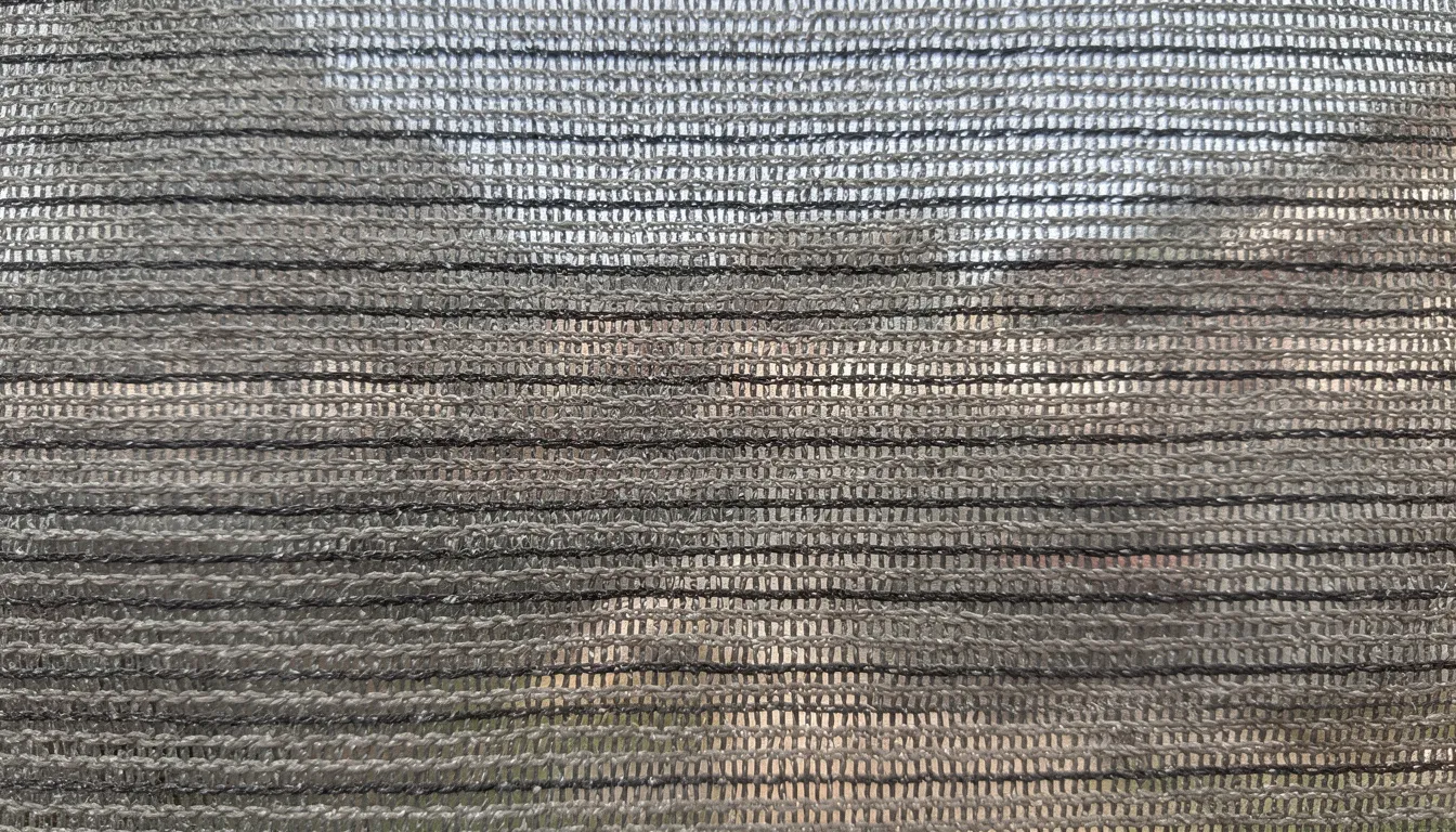 The image showcases a close-up view of solar shade fabric, highlighting its intricate woven pattern that allows for partial visibility while effectively blocking harmful UV rays. This texture is ideal for high ceiling windows, providing light control and enhancing the airy atmosphere of modern living spaces.