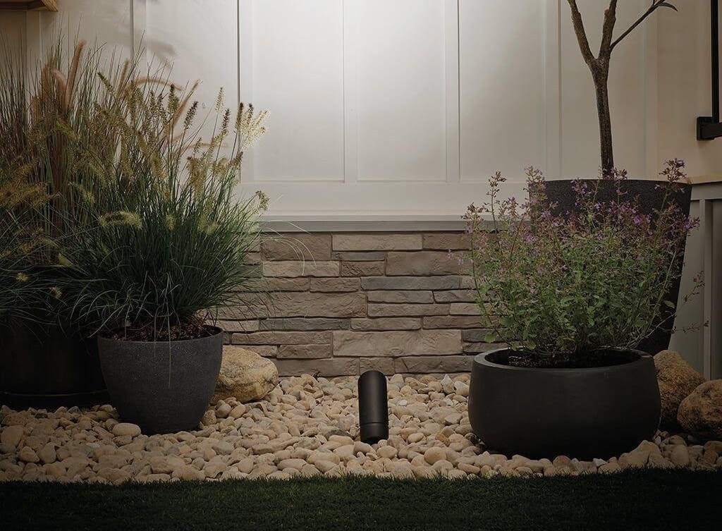 Outdoor lighting trends showcasing a spotlight fixture in a landscaped garden with stone accents, enhancing the space with warm illumination.