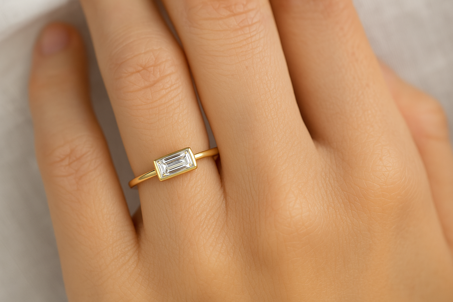 Sužadėtuvių žiedas su baguette formos deimantu geltoname aukse ant moters bevardžio piršto.