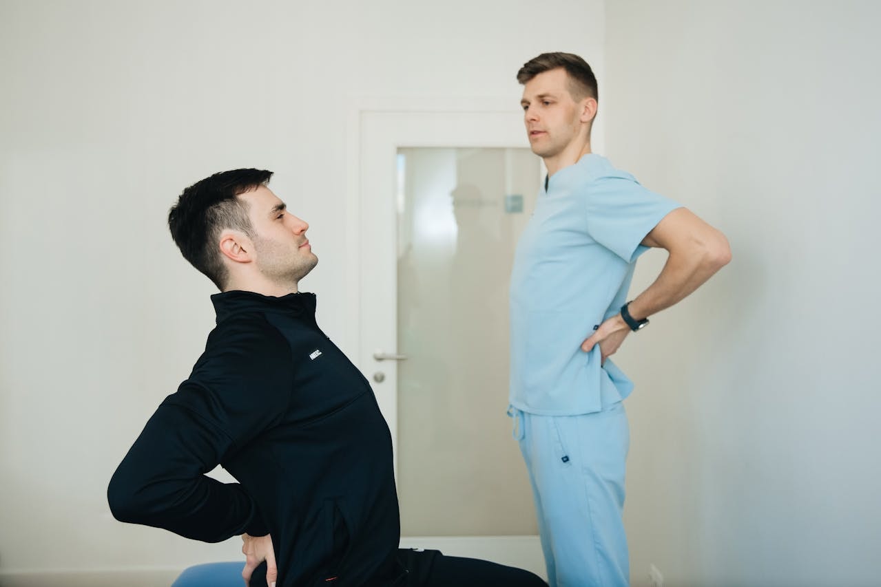 Stretching exercises for the spine as a patient practices a gentle back extension while a physical therapist coaches posture in a clinic.