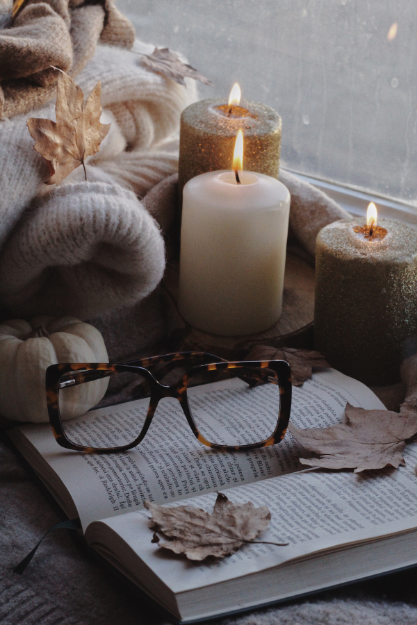 a cozy fall interior with candles, sweaters, book, and glasses