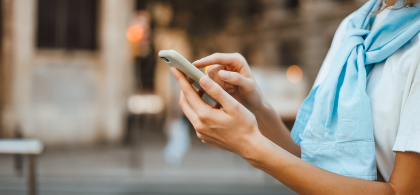 Woman with a blue sweater tied around her neck checking her cell phone. 