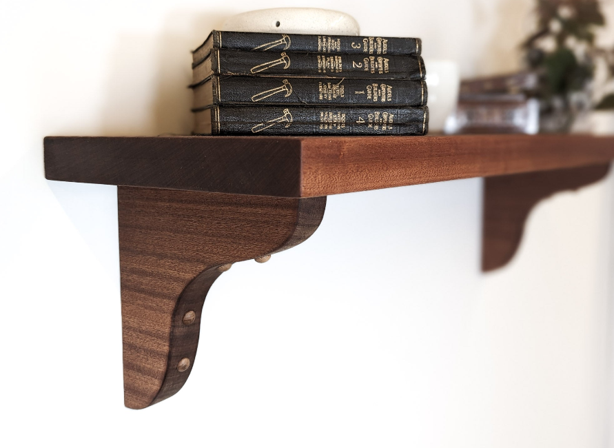 A mahogany shelf with brackets, four books lay on top of one another on their side. 