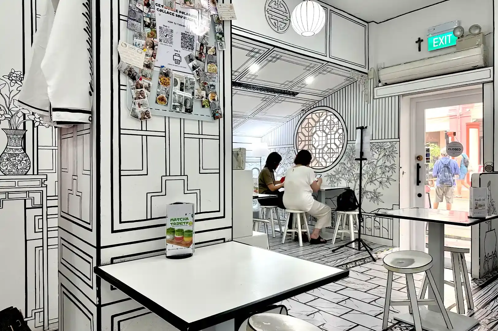 Patrons dining inside Singapore's first 2D cafe, Cafe Monochrome, surrounded by walls and furniture painted with hand-drawn comic book line art.