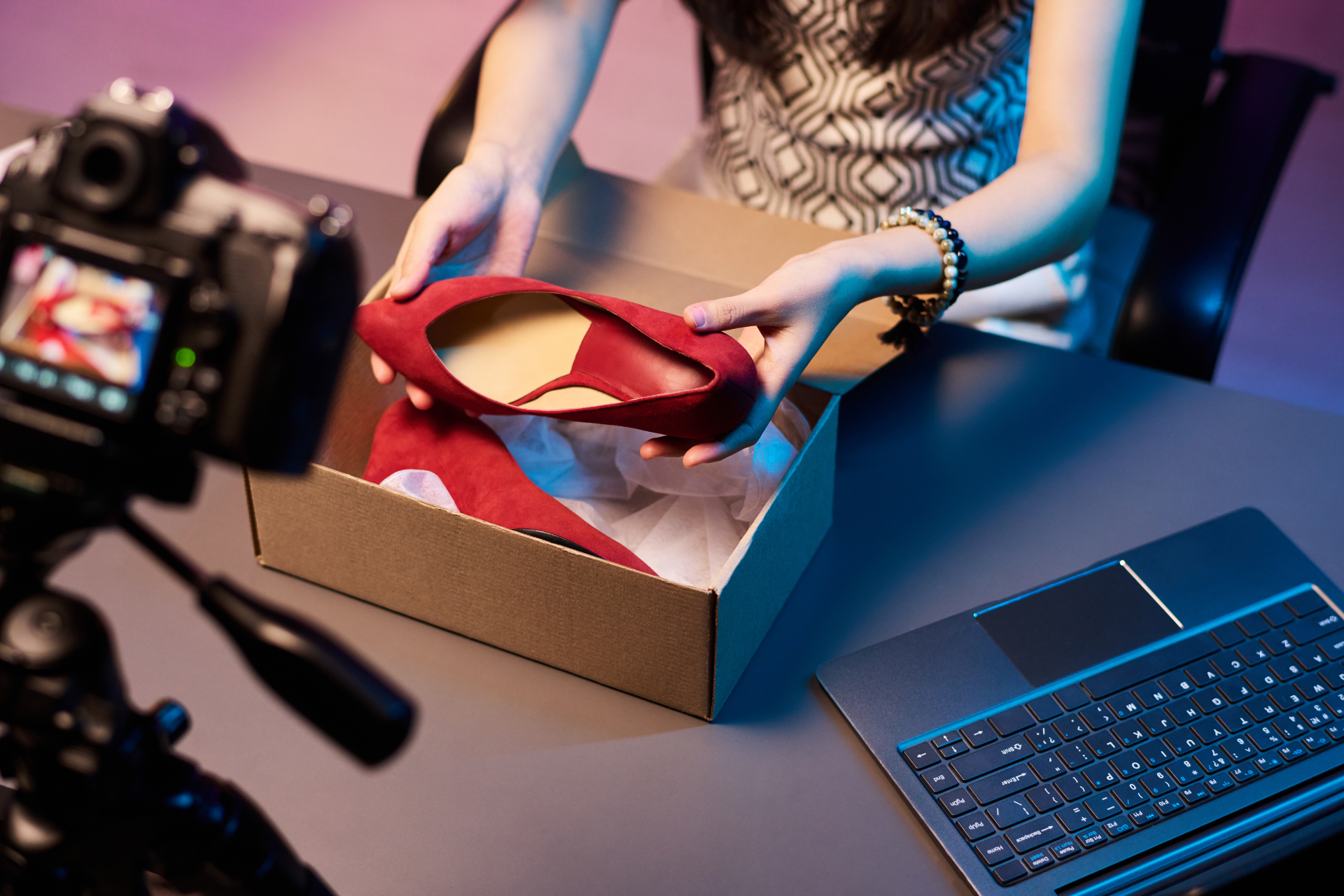 A content creator unboxing a red high-heel shoe from a box while being filmed by a DSLR camera in a studio setting.