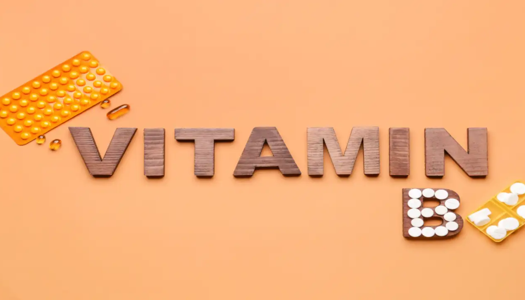 Trebokstaver som staver “VITAMIN B” med piller og kapsler rundt på oransje bakgrunn som symboliserer vitamintilskudd.