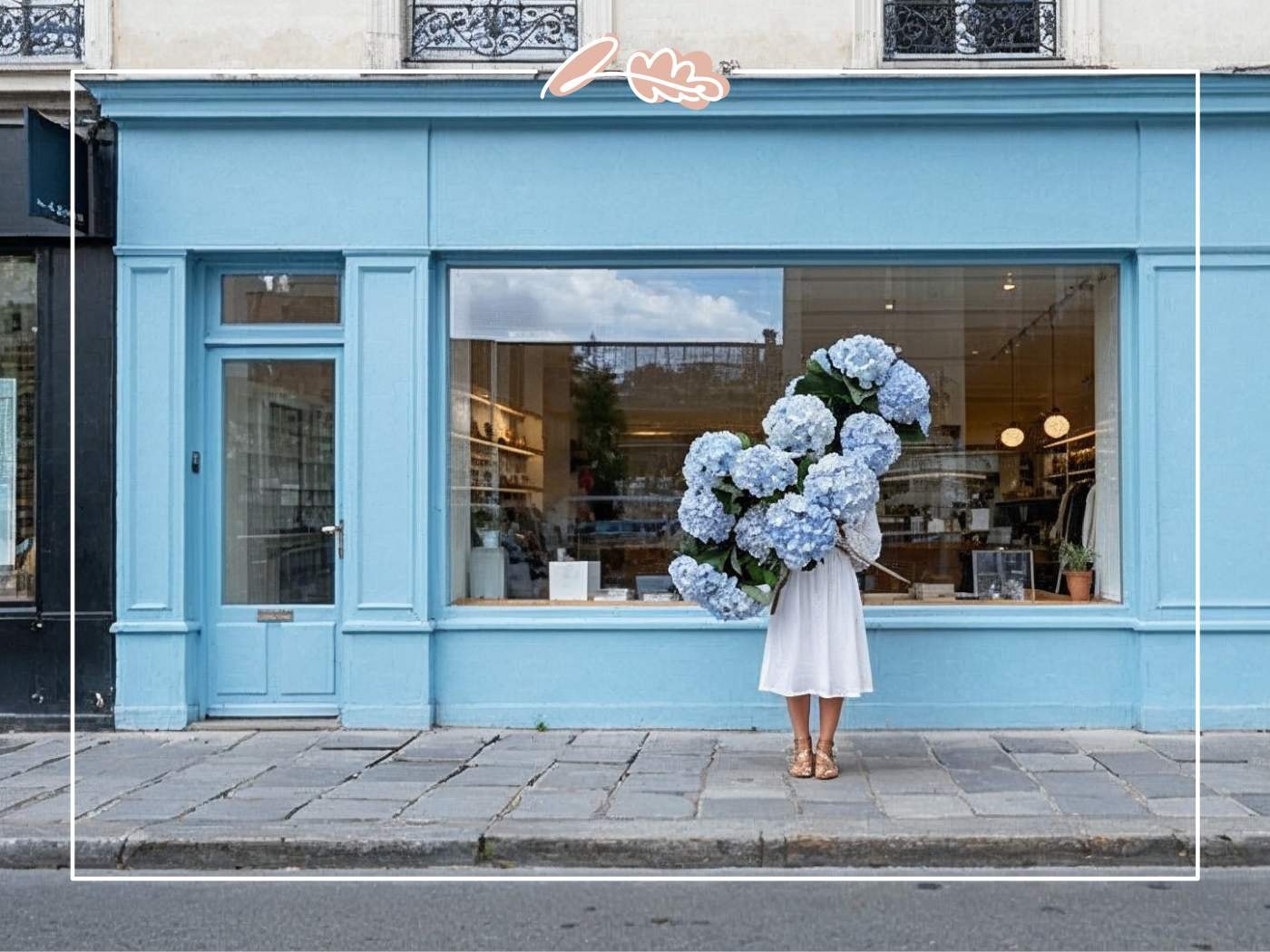 Woman holding a large bouquet of fresh blue hydrangea blooms outside a pastel blue flower shop