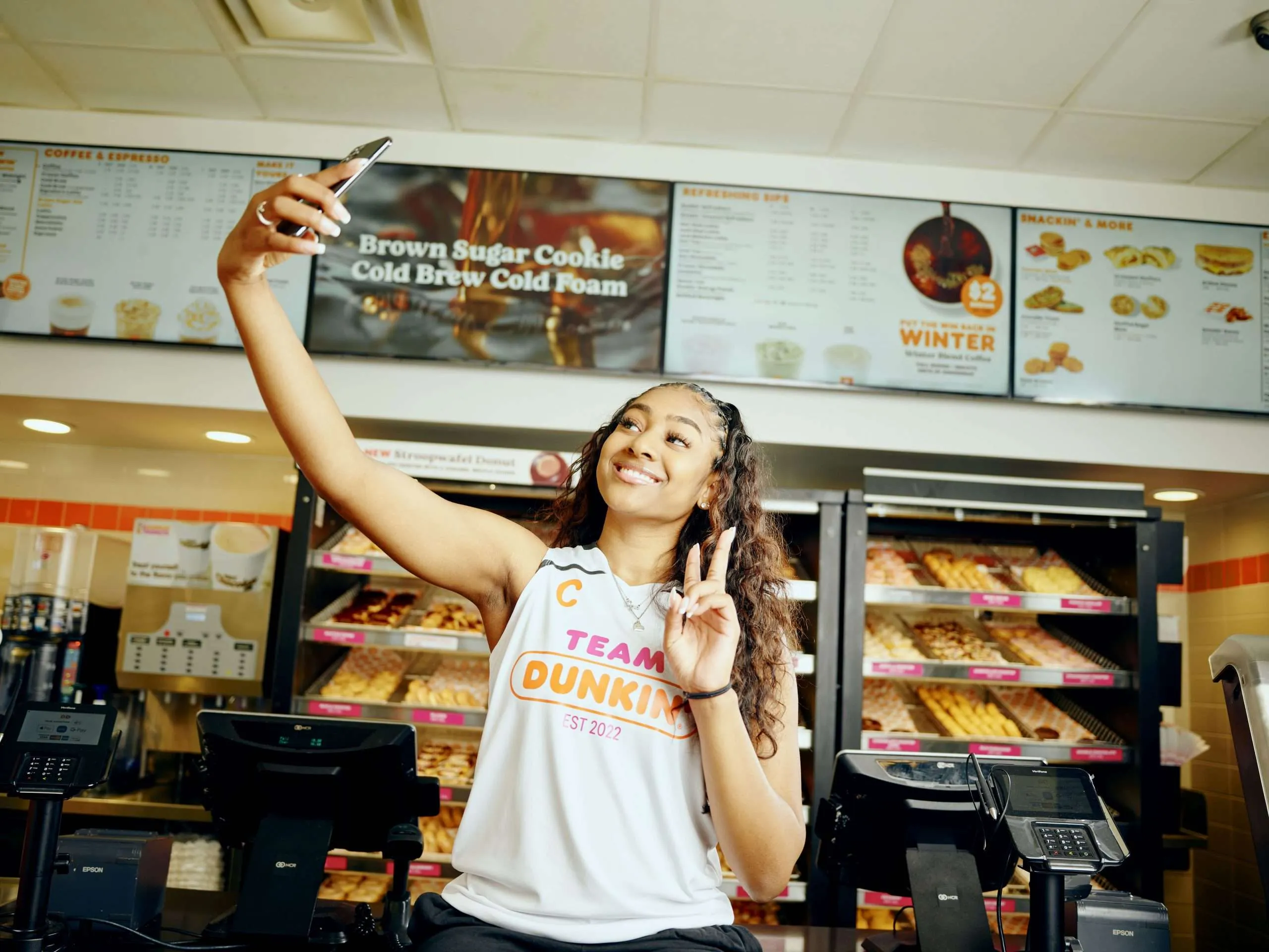 Basketball player Deja Kelly taking a selfie at a Dunkin' store, showcasing her NIL endorsement with Team Dunkin'.