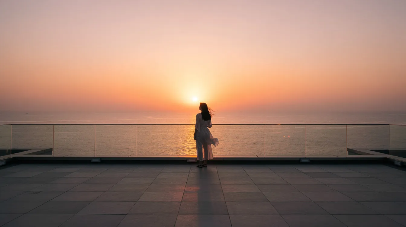 Die Silhouette einer einzelnen Person steht auf einer großen Dachterrasse über dem Meer, während die Sonne am Horizont untergeht und eine kontemplative Stimmung erzeugt. Diese Szene erinnert an die filmischen Werke von Jean-Luc Godard, in denen die Verachtung für das Kommerzielle oft thematisiert wird.