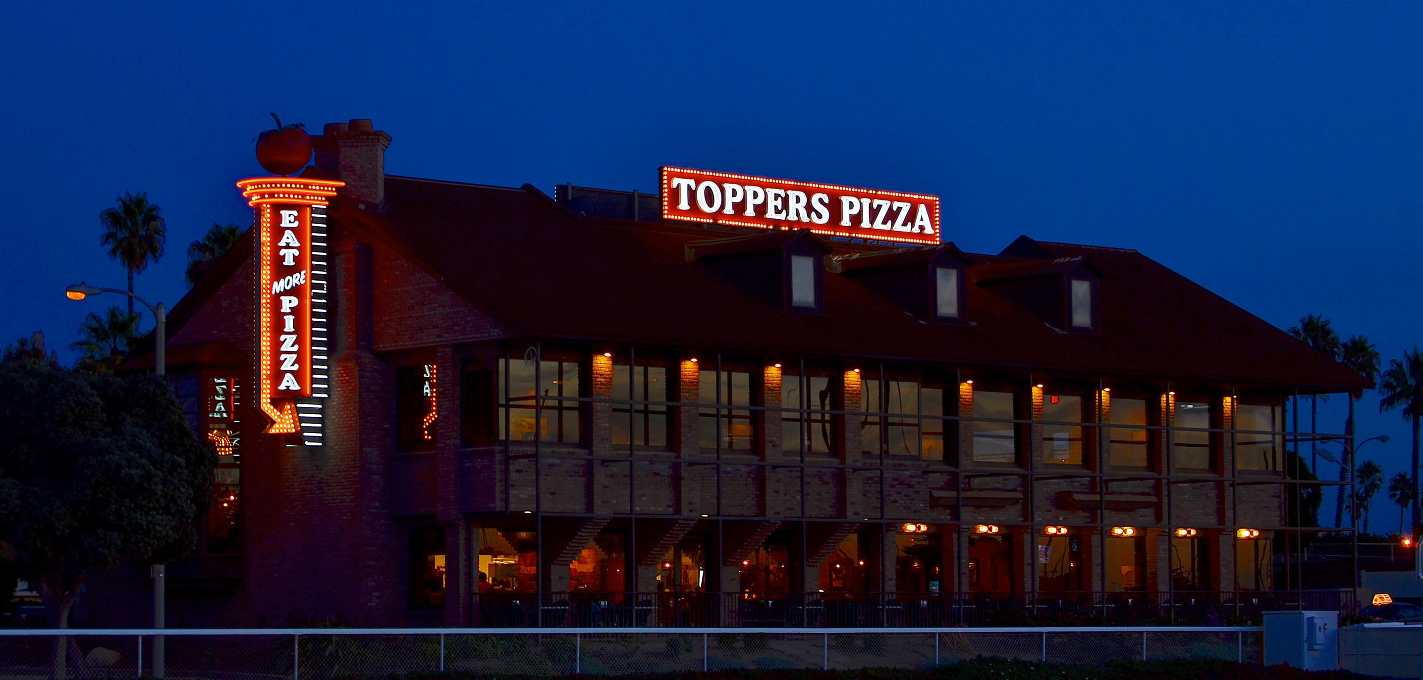 Custom signage for Toppers Pizza at the Harbor includes bold rooftop lettering that lights up the waterfront and the iconic “Eat More Pizza” sign welcoming guests at the entrance.