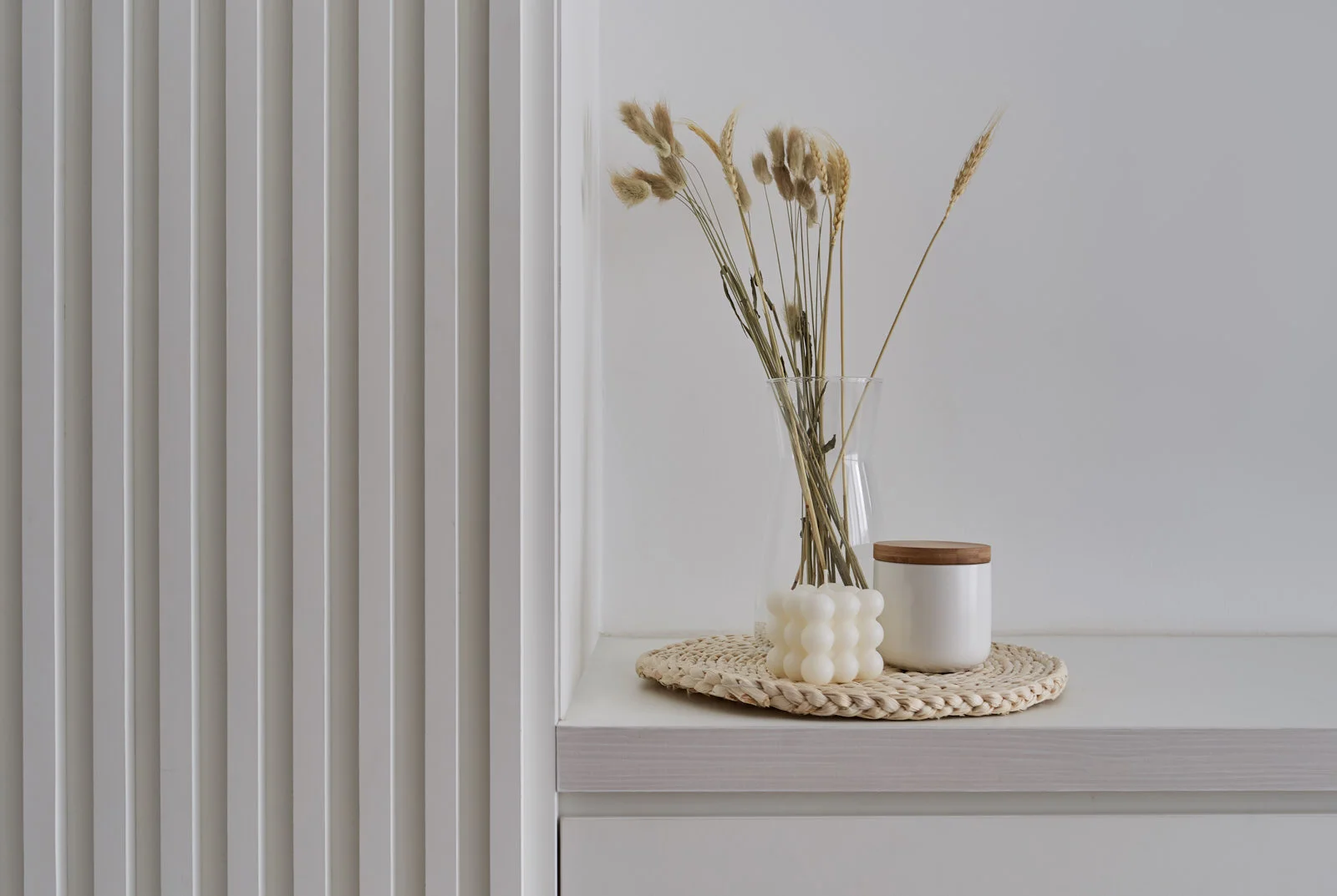 Minimalist interior design detail – dried florals and sculptural candle on fluted white console.