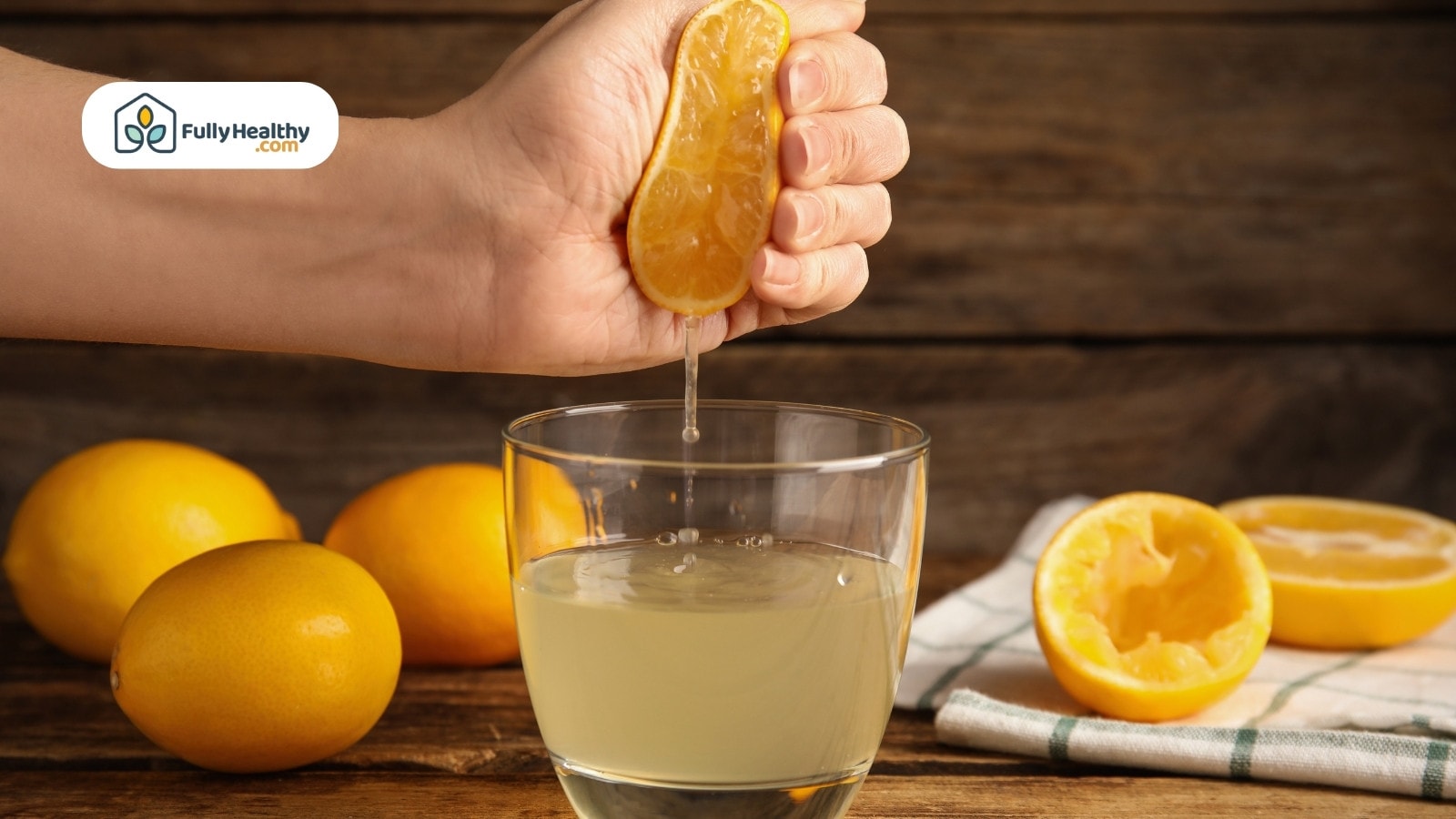Hand squeezing lemon juice into glass on rustic wooden table