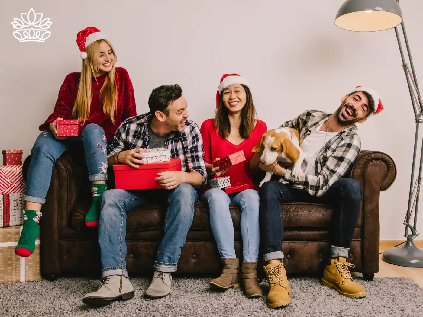 A group of friends sitting on a couch, joyfully holding gift boxes and a beagle dog, with more presents stacked nearby, part of the Festive Season Gift Boxes Collection. Delivered with Heart by Fabulous Flowers and Gifts.