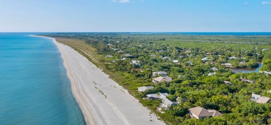 An aerial view showcases the luxurious Gulf Pines homes surrounded by lush tropical vegetation, with the stunning Gulf of Mexico visible in the background. This serene setting in Sanibel Island highlights the private beach access and beautifully crafted living spaces that define the Gulf Pines community.