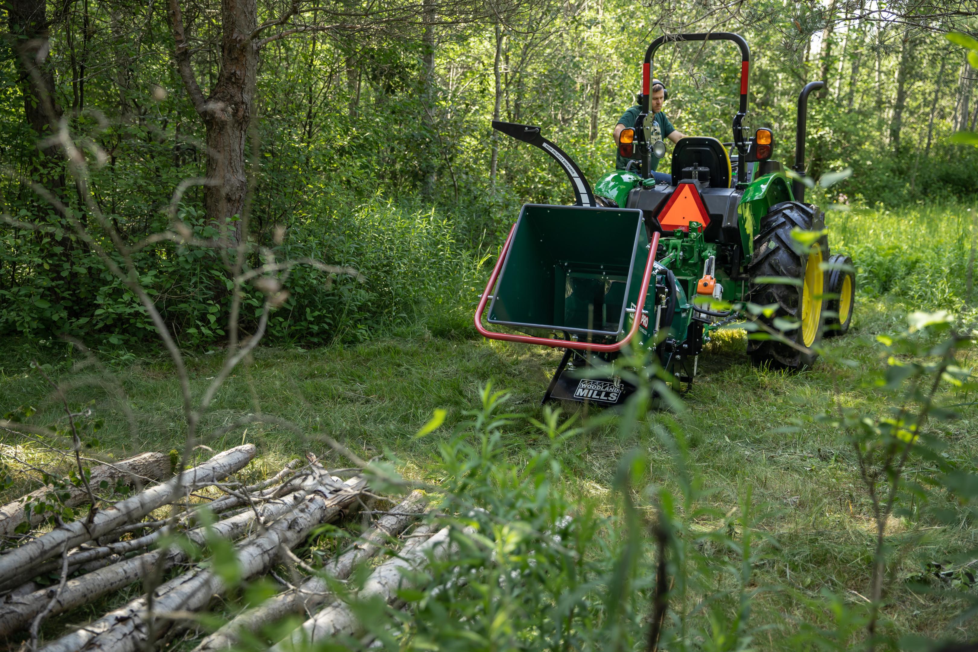 A stack of trees ready to be chipped in front of a Woodland Mills TF810 PRO Wood Chipper.