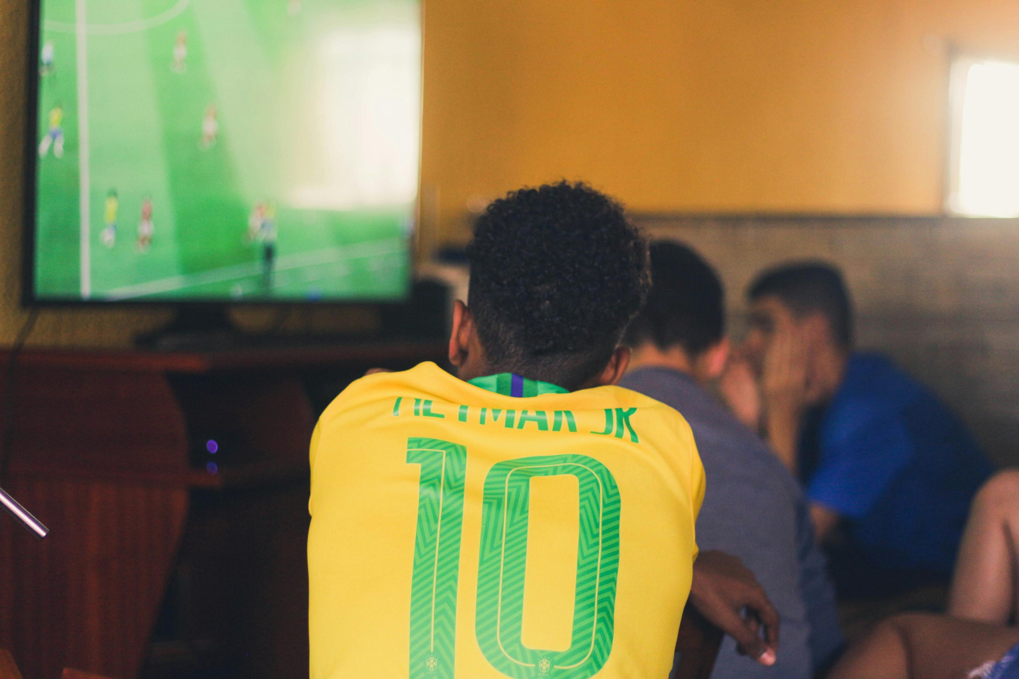 Image of a man in a Brazilian Jersey watching a soccer match.