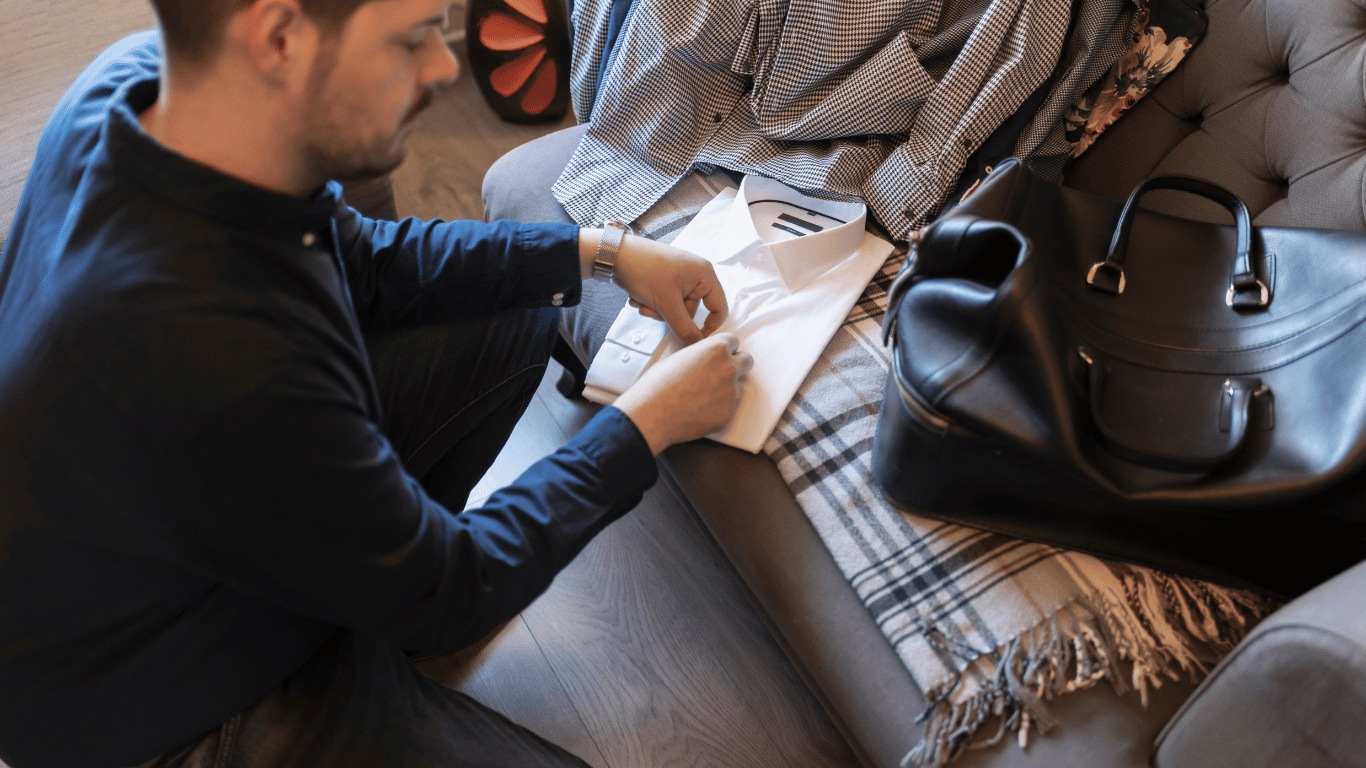 man folding clothes beside his weekender bag