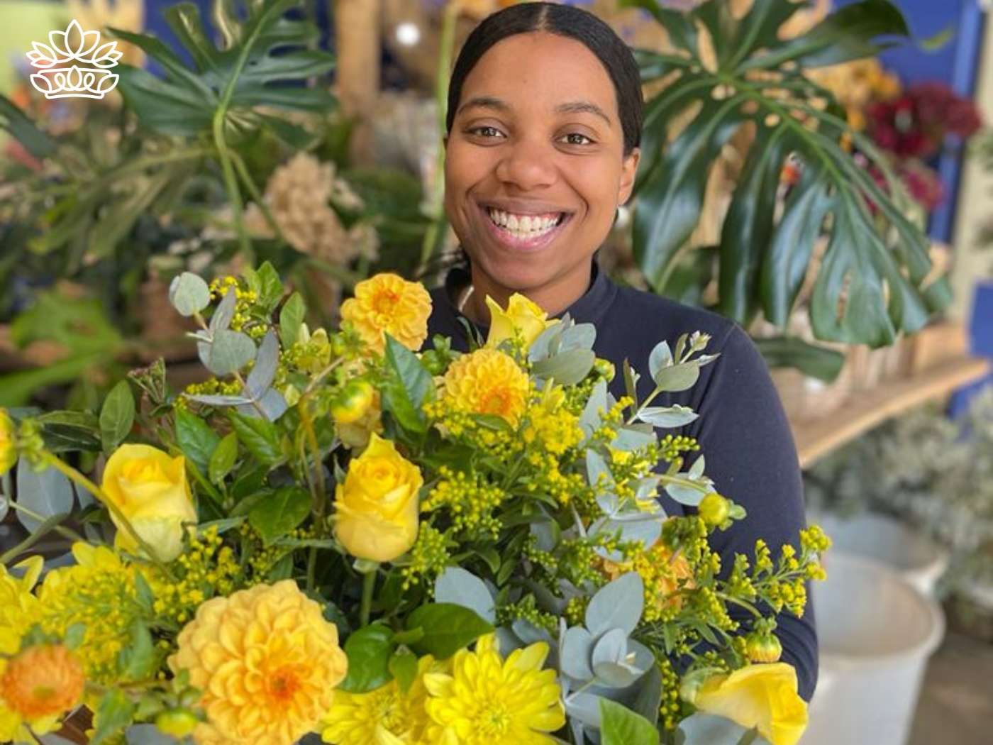 Alt text: "A radiant young woman with a warm smile holds a vibrant bunch of yellow roses and complementary colourful flowers at a florist shop, symbolising the cheerful essence of life. Fabulous Flowers and Gifts.