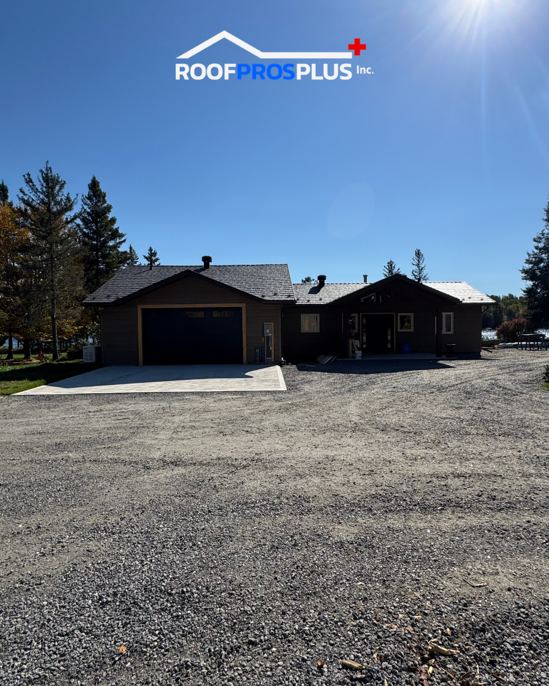 A house with a grey metal roof, surrounded by a gravel driveway and a large gravel parking lot for vehicles.