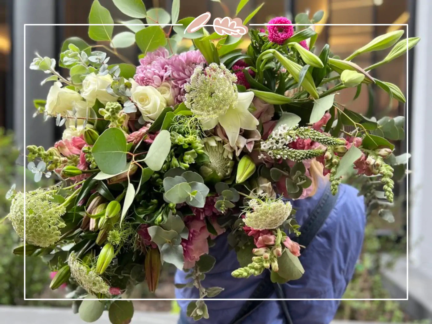 A close-up of a person holding a lush and diverse bouquet of green, white, and pink flowers outdoors.