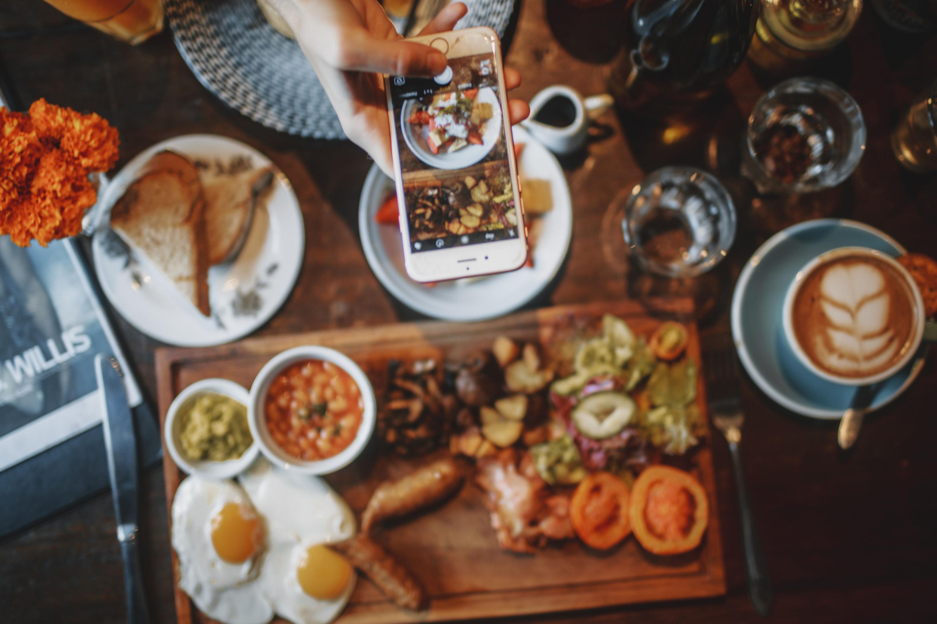 A smartphone screen displays a vibrant food delivery order being placed, with a finger poised to tap the screen. This scene captures the convenience of ordering from a restaurant, highlighting the growing trend of using social media platforms for restaurant marketing and engaging local customers.