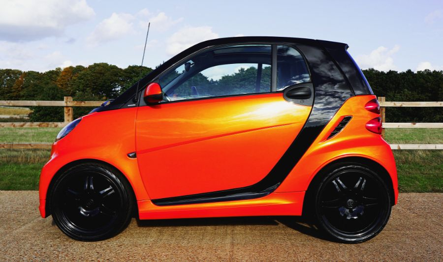 Pomarańczowy microcar (mikrosamochód) w nietypowym dla siebie, wiejskim otoczeniu.