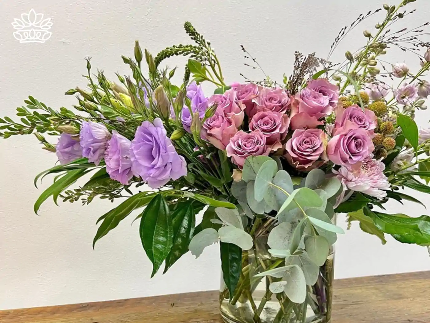 Elegant flower arrangement in a glass vase featuring soft pink roses, lavender lisianthus, and assorted greenery, exuding sophistication and charm. Fabulous Flowers and Gifts: Flower Arrangements Under R500, Delivered with Heart.