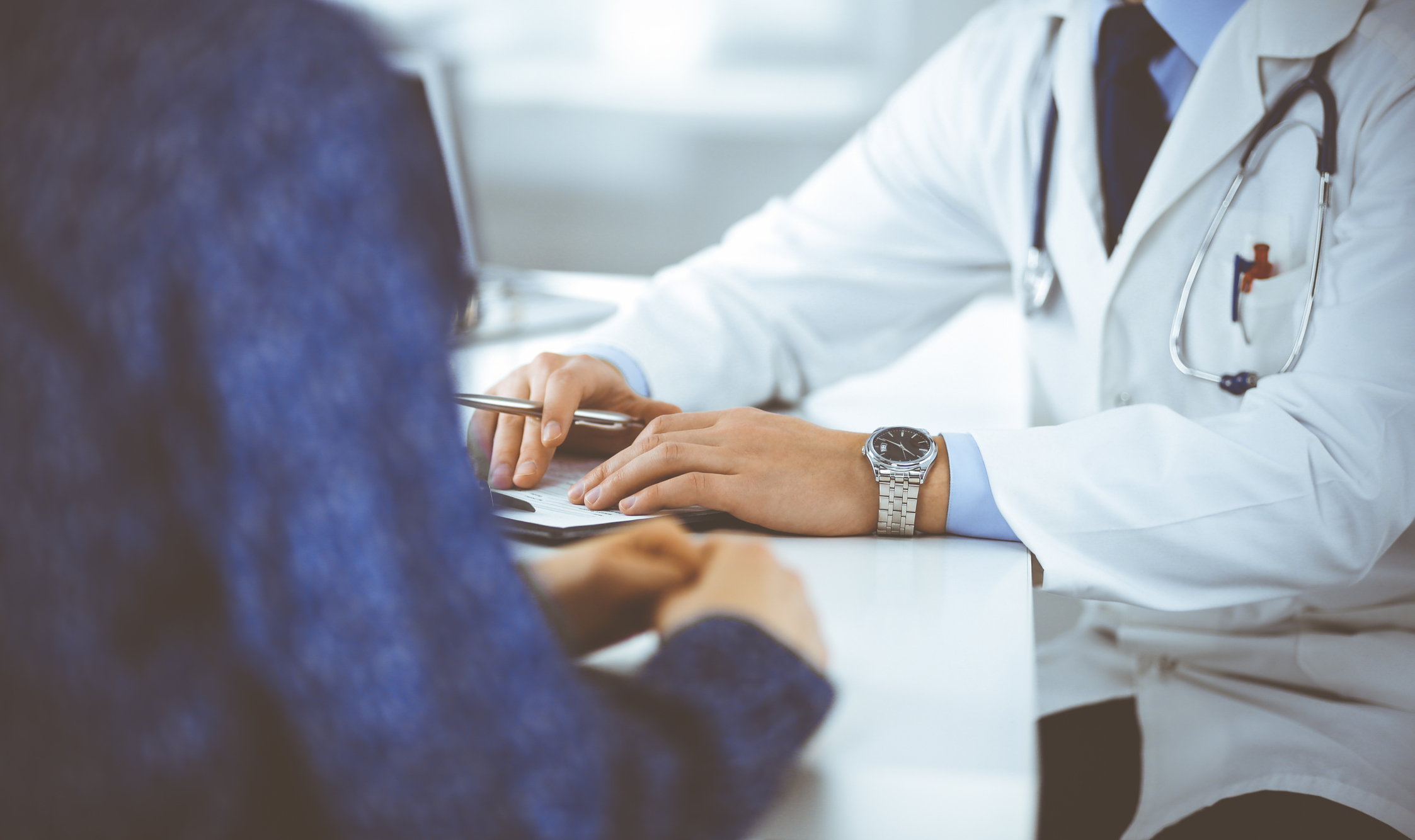 An image of a doctor consulting with a patient at his desk. 