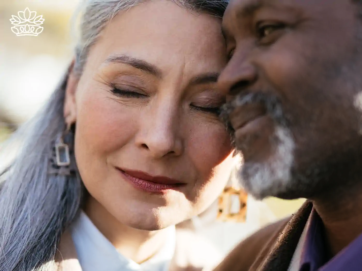 Close-up of a tender moment between a mature couple, a Caucasian woman and an African American man, sharing a gentle forehead touch, reflecting love and empathy. Funeral Flowers from Fabulous Flowers and Gifts.