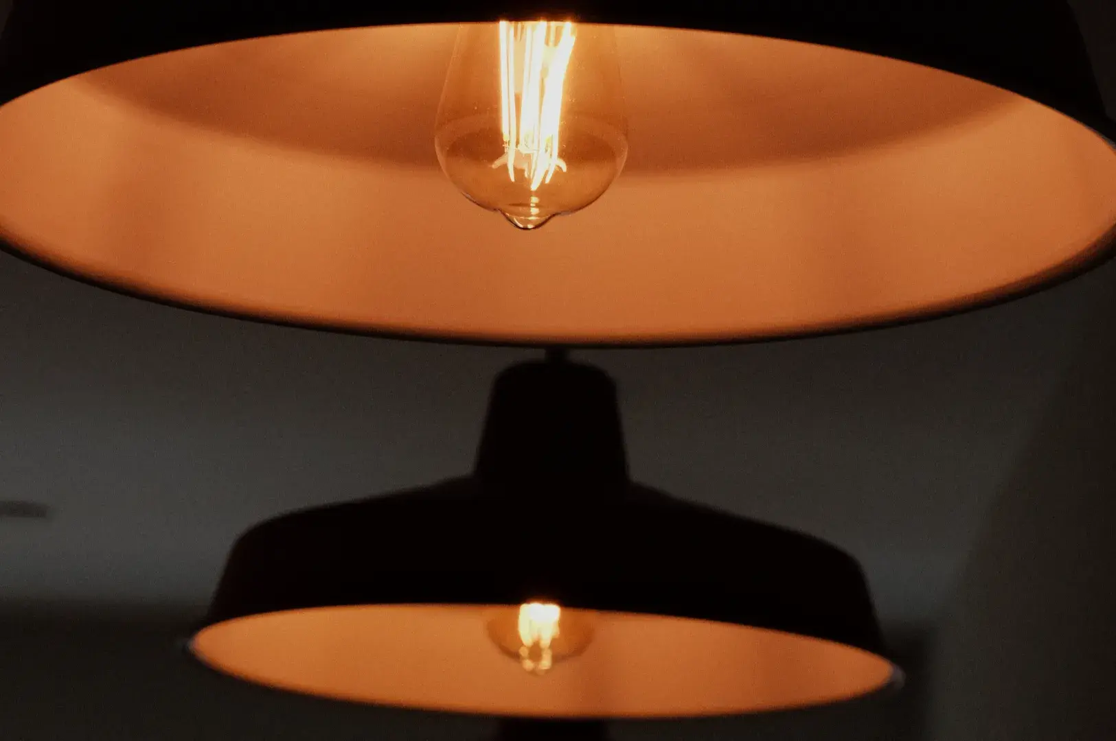 Two pendant lights with warm-toned shades, casting a soft glow in a dimly lit environment.