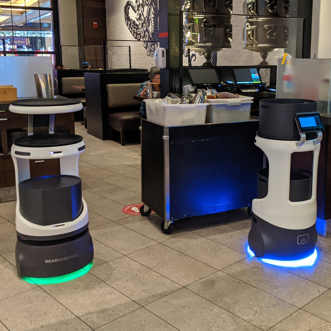 Two Servi robots with LEDs at the front of a restaurant.