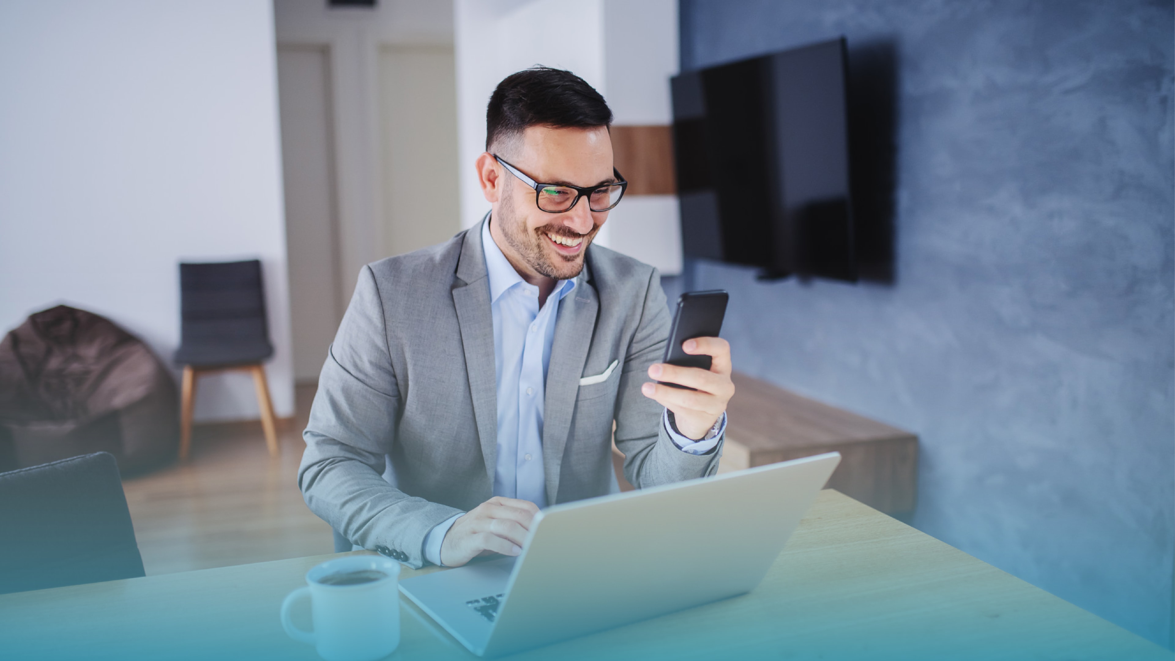 Smiling man in a suit using his phone while working on a laptop, showing strong internet connection through fiber optic internet.