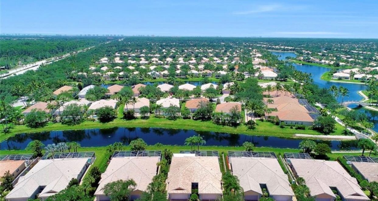 The image showcases a resort-style pool area featuring a lap pool and a leisure pool, surrounded by modern pool deck furniture and lush palm landscaping, creating an inviting outdoor living space for residents of the desirable Island Walk community in North Naples. This vibrant setting is perfect for relaxation and enjoyment, embodying the Southwest Florida beach lifestyle.