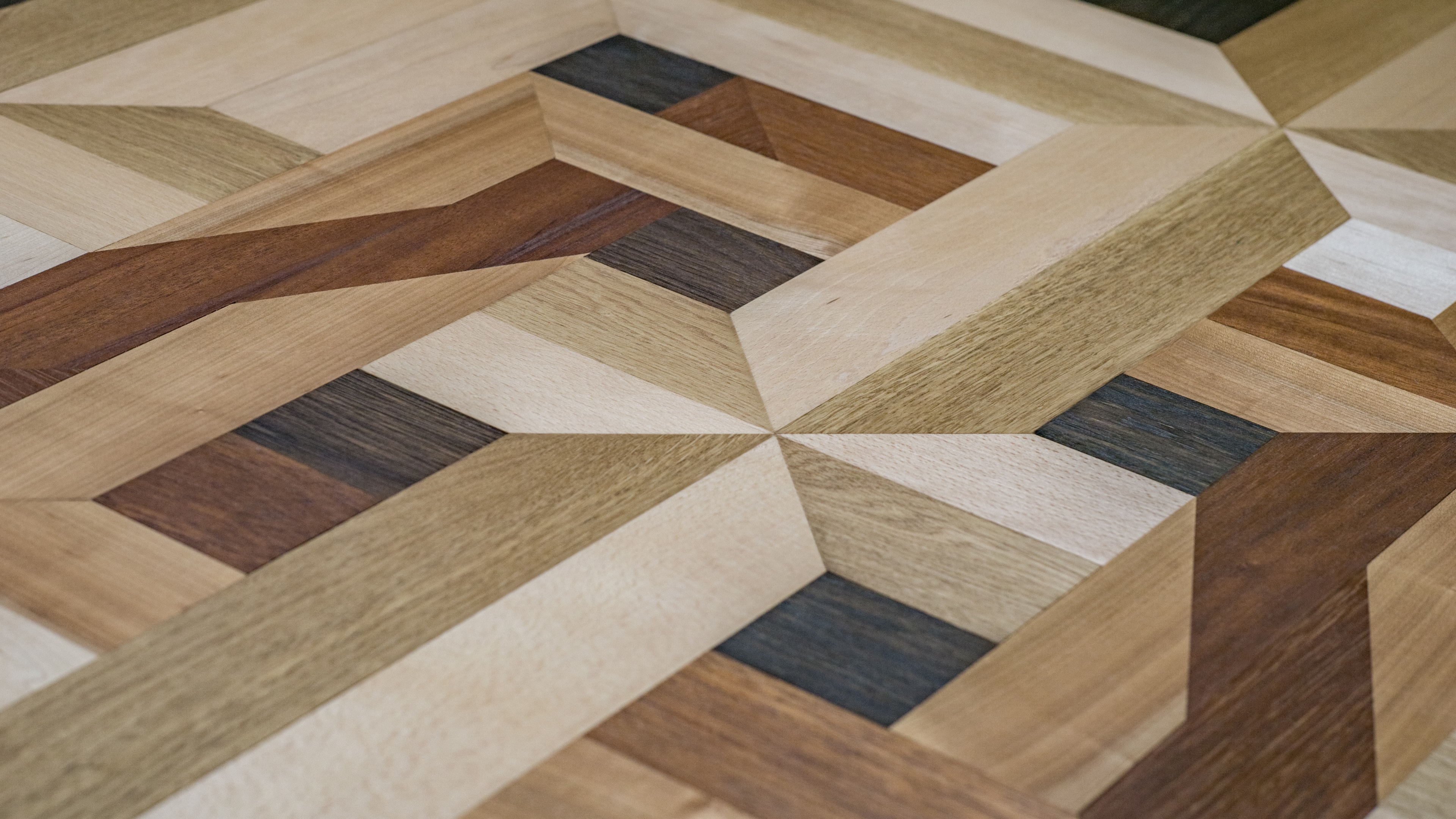 Detailaufnahme eines Intarsien-Parkettbodens mit verschiedenen Holzarten und geometrischem Muster