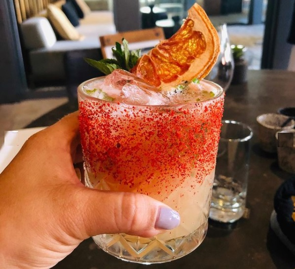someone holding an orange cocktail garnished with ice and fruit