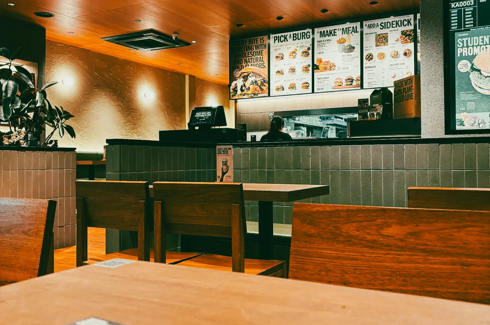 : Eye-level shot of a casual halal fast-casual restaurant with wooden seating, counter ordering area, and illuminated menu boards in a warm, contemporary setting.