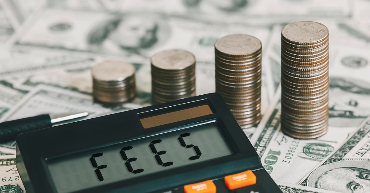 Stacks of coins and dollar bills next to a tax preparation fee calculator displaying the word 'Fees'.