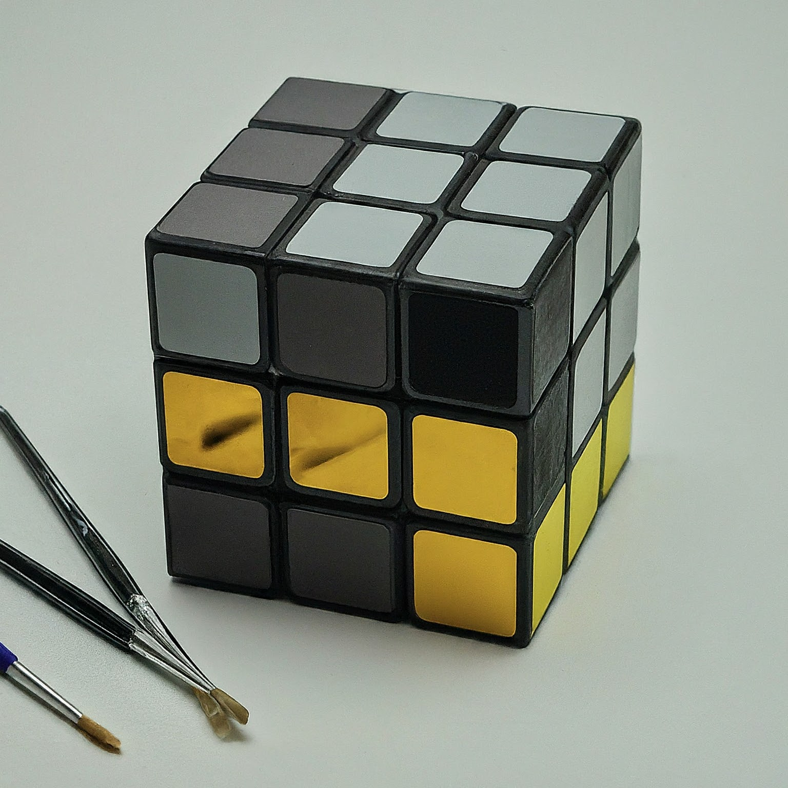 A classic Rubik's cube with a white background. The cube's sides are a mix of golden grey and black shades. 