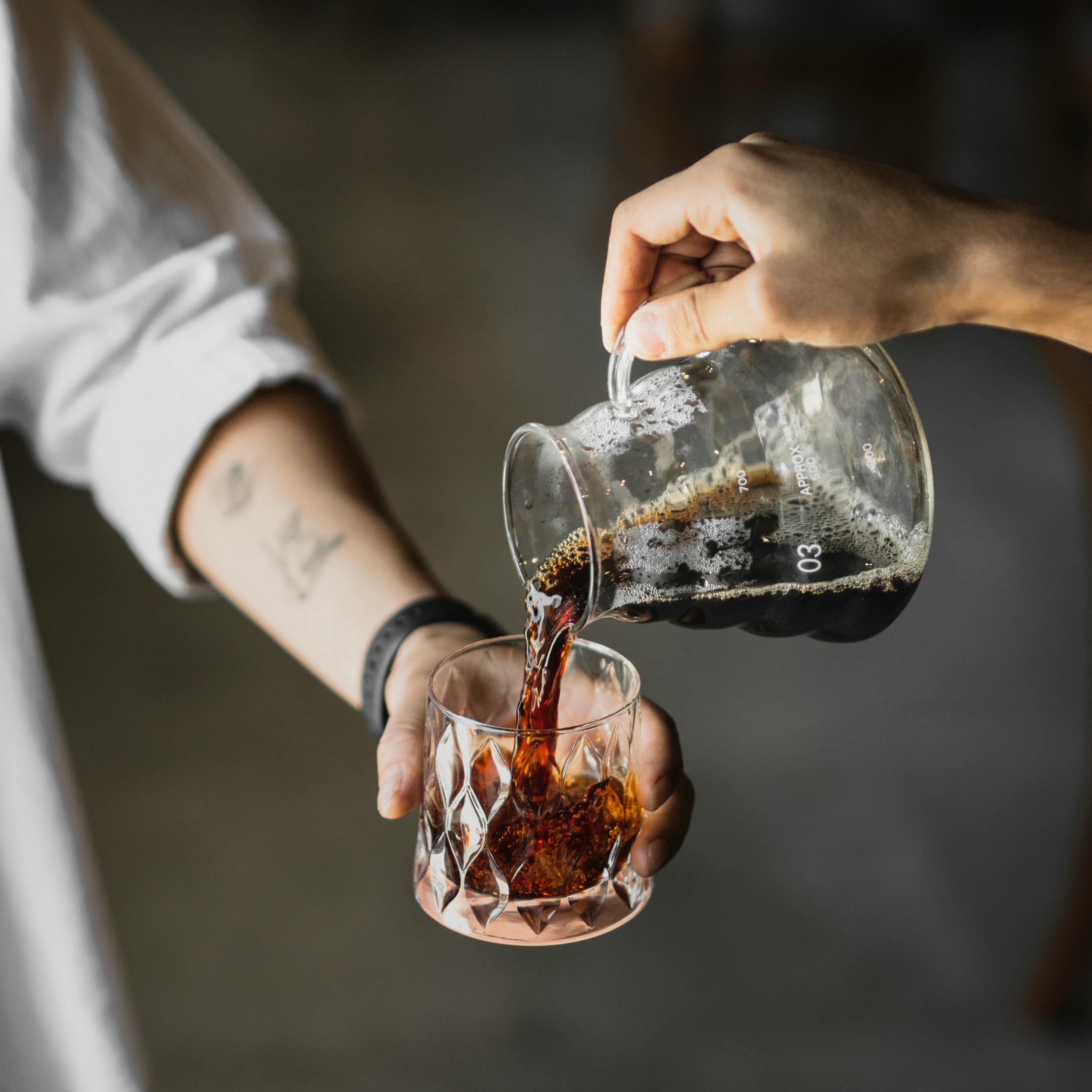 pouring cold brew from coffee pitcher into a clear glass