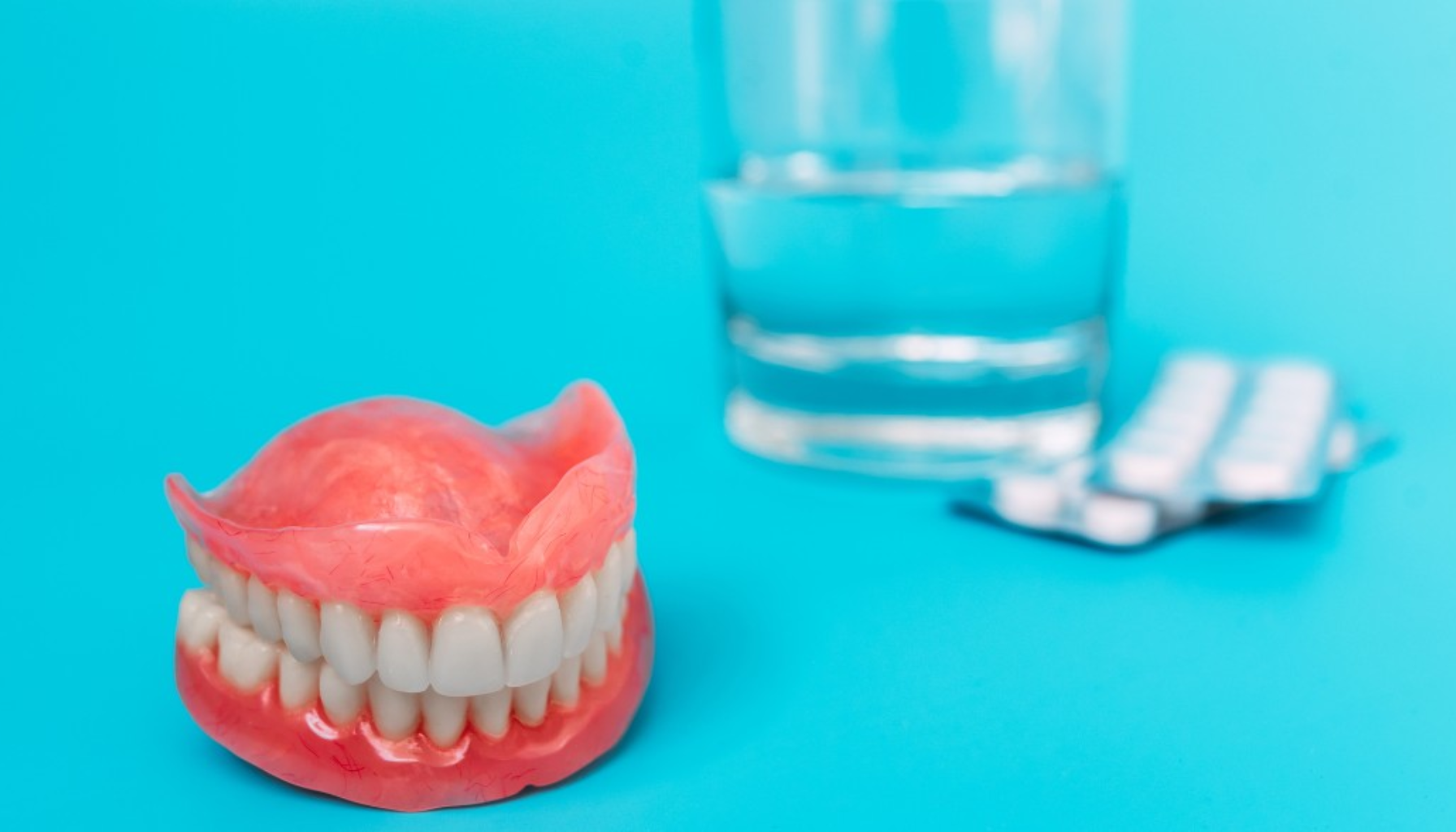 Gebiss – En komplett guide til avtakbare tannproteser 15 Protese med gebiss plassert foran et glass vann og medisinbrett på blå bakgrunn.