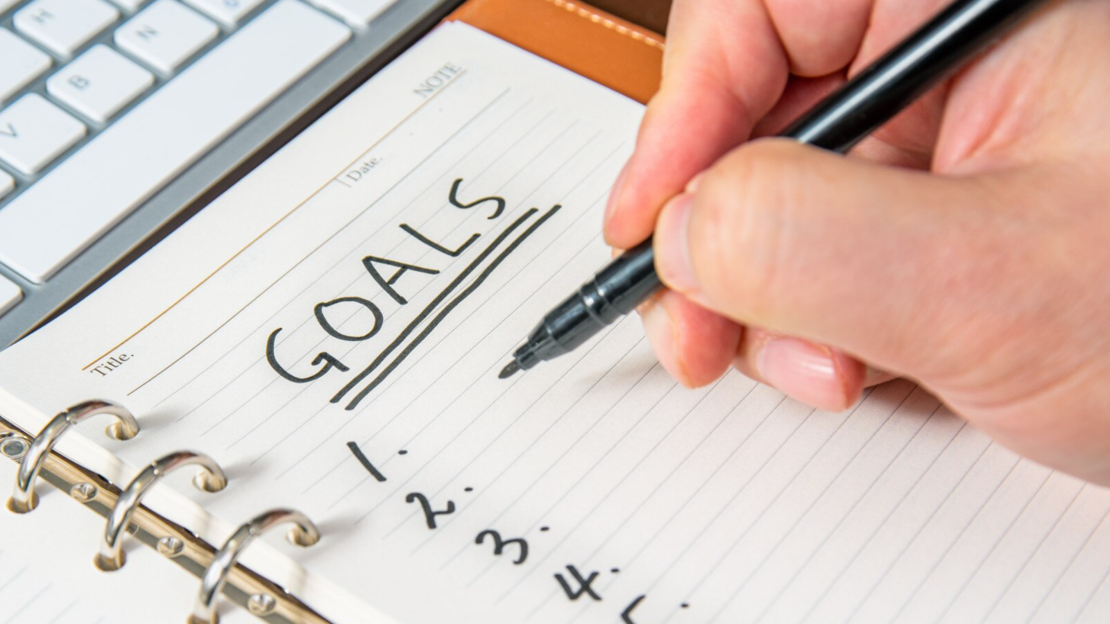 A hand writing a list of content marketing goals list in a notebook.